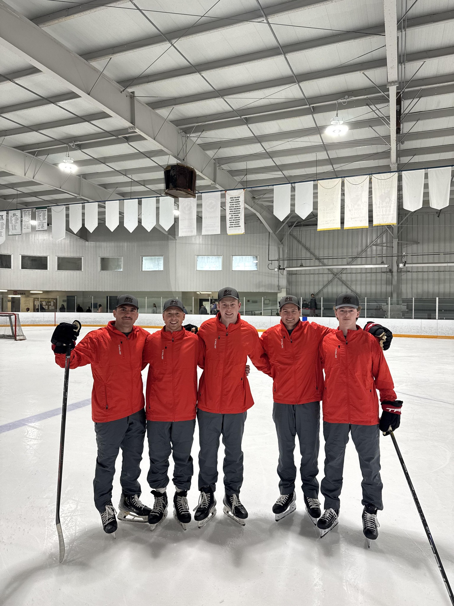 coaches - Fresh Legs Hockey School Five hockey players in red jackets stand together on an ice rink, arms around each other, posing for a team photo with sticks